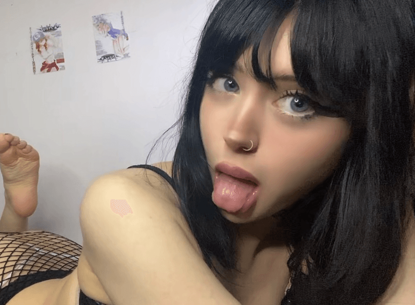 Close-up portrait of a person with black hair and a nose ring, sticking out their tongue toward the camera.