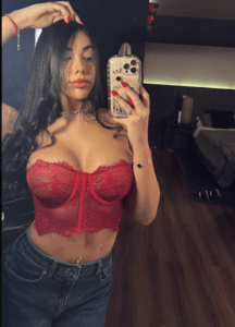 Woman taking a mirror selfie in a red lace bralette and jeans, in a modern bedroom backdrop.
