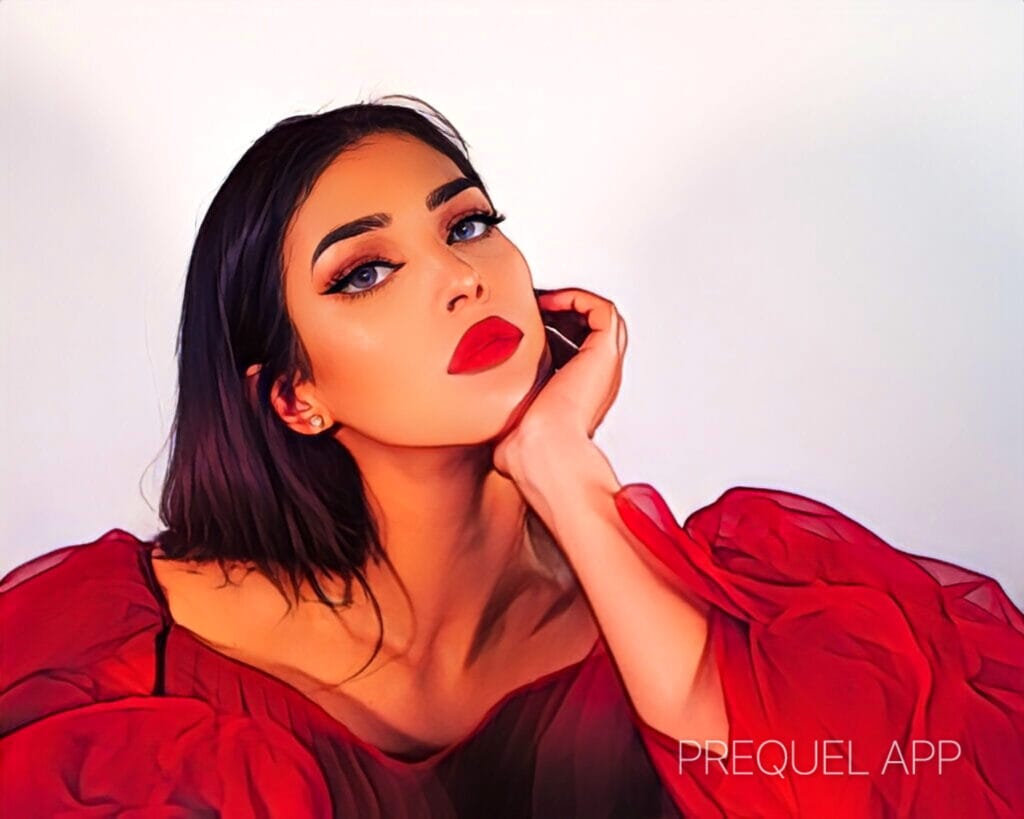 Close-up portrait of a woman with bold makeup and red lipstick, resting her chin on her hand in a sheer red dress.