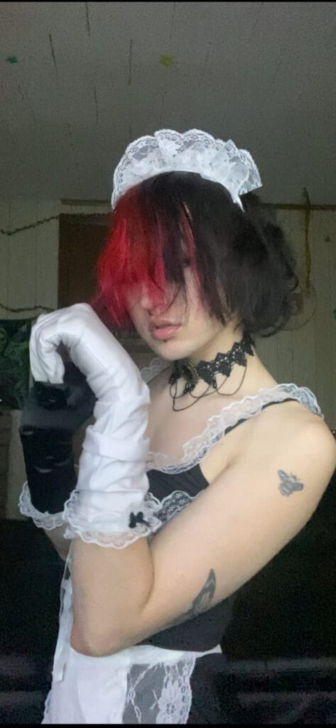 Person wearing a lace maid costume with white gloves and a lace headpiece on a dark background.